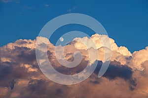 Small moon above large, storm cloud, during the day