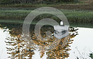 A small motor boat in a lake with trees reflecting in the water