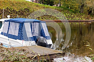 A small motorboat with a blue tarpaulin cover is parked on the water at the wooden pier