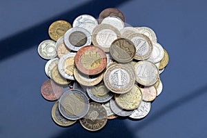 A small mountain of coins from different countries on a blue background.