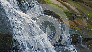 A small mountain stream with fast moving clear water between rocky stones in autumn.