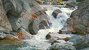 A small mountain stream with fast moving clear water between rocky stones in autumn.