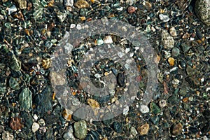 Small multicolored stones on the bank of a mountain stream with crystal clear glacial water. Top view.