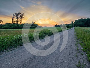 Small narrow road in a country side without asphalt at sunset, stunning colorful sky. Nobody. Nature scenery. Latvia rural area