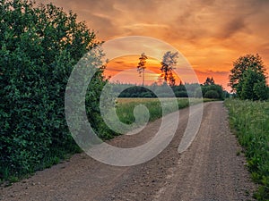 Small narrow road in a country side without asphalt at sunset, stunning colorful sky. Nobody. Nature scenery. Latvia rural area
