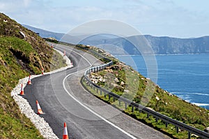 Small narrow road by the ocean, Achill Island, county Mayo, Ireland. Warm sunny day. Irish landscape. Blue clear cloudy sky.