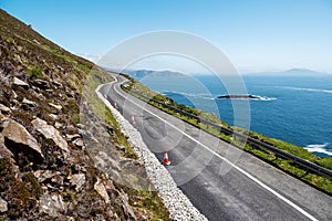 Small narrow road by the ocean, Achill Island, county Mayo, Ireland. Warm sunny day. Irish landscape. Blue clear cloudy sky.