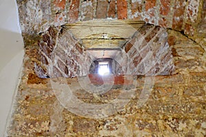 A small narrow window on an old, ancient, cracked stone shabby brick wall of red brick in the basement. The background