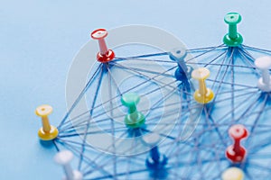 Small network of colorful pins and string, An arrangement of colorful pins linked together with string on a blue background