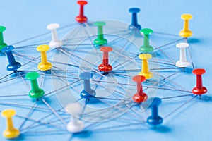 Small network of colorful pins and string, An arrangement of colorful pins linked together with string on a blue background