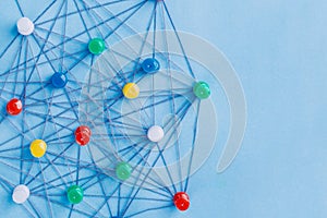 Small network of colorful pins and string, An arrangement of colorful pins linked together with string on a blue background