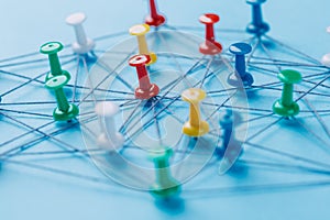 Small network of colorful pins and string, An arrangement of colorful pins linked together with string on a blue background