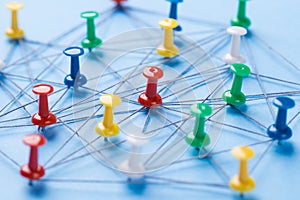 Small network of colorful pins and string, An arrangement of colorful pins linked together with string on a blue background