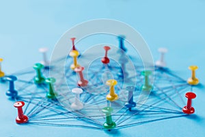 Small network of colorful pins and string, An arrangement of colorful pins linked together with string on a blue background