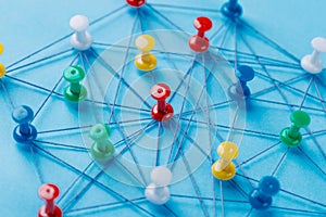 Small network of colorful pins and string, An arrangement of colorful pins linked together with string on a blue background