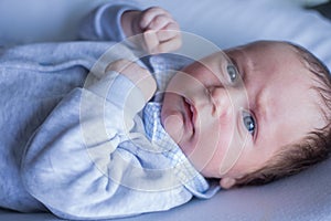 A small newborn baby with blue eyes clenching his fists and taking a boxing pose lies in a gray suit with a checkered