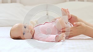 a small newborn baby girl lies on a white cotton bed at home, mother's hands stroke or do foot massage