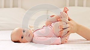 a small newborn baby girl lies on a white cotton bed at home, mother's hands stroke or do foot massage