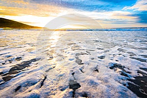 Small ocean sea waves on sandy beach with sunrise sunset.