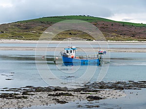 A small old fishing boat is anchored, shallow water at low tide on day