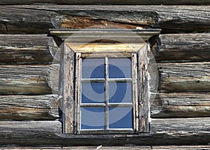 Small Old window with glass with a blue sky on the background of the wooden wall of the countryside log house