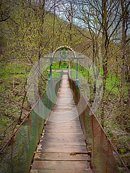 Small old wooden bridge over the mountain river. Beautiful mountain landscape with dry trees and earth covered with green grass.