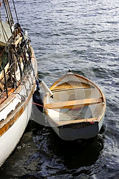 Small old wooden rowing boat moored with rope to a historical white sailboat as a rescue boat for nautical concept,