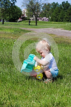 Small one year old boy child playing with toy truck car in the park