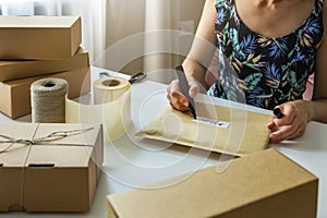 Small online store owner writing envelope shipping label at home for shipment delivery