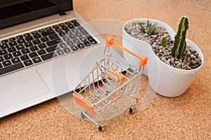 A small orange cart stands next to a laptop this image implies online shopping