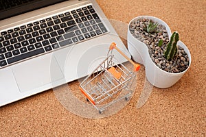 A small orange cart stands next to a laptop, a phone, and a cactus.