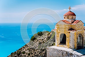 Small orange colored Hellenic shrine Proskinitari on the cliff edge with defocused sea view in the background