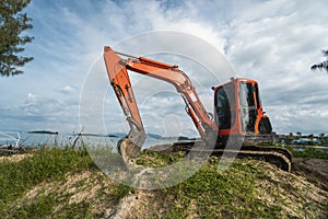 Small orange excavator on a ground against blue sky and sea for a works on construction site. Small tracked excavator