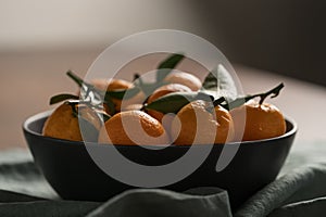 Small organic tangerines with leaves in ceramic bowl on wood table