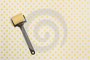 A small paint roller on a background with yellow polka dots