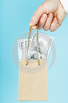 A small paper bag for financial aid and support made of paper at arm`s length with US dollars on a blue background. The concept o