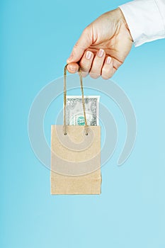 A small paper bag for financial aid and support made of paper at arm`s length with US dollars on a blue background. The concept o