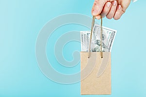 A small paper bag for financial aid and support made of paper at arm`s length with US dollars on a blue background. The concept o