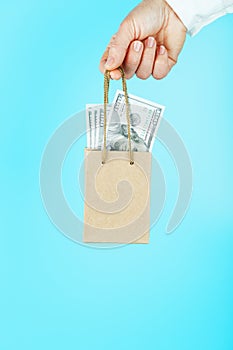 A small paper bag in hand with US dollars on a blue background. Layout of the packaging template with space for copying,