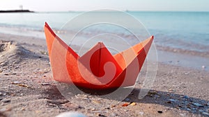 Small paper orange boat on sand near water on background of sea waves close-up.