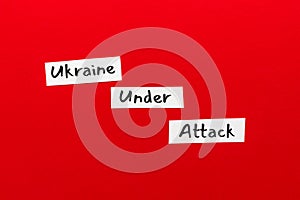 Small paper pieces with text UKRAINE UNDER ATTACK on on RED background. No war, stop aggression, stop putin. photo