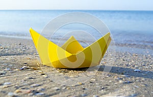 Small paper yellow boat on sand near water on background of sea waves