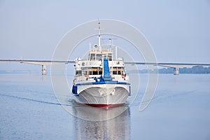 Small passenger motorship on the river and road bridge in the morning haze in the background