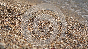 Small pebbles or rough sand beach, lit by sun, sea water washes over, closeup detail - abstract shallow depth of field tropical