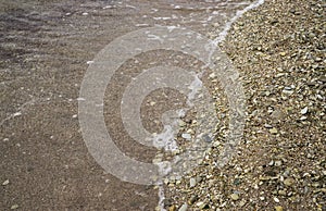 Small pebbles and wet sand on the sea beach; water line.