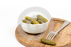 Small pickles in the white bowl and pickle on the fork