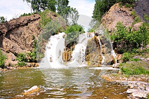 A small picturesque waterfall flowing down between the mountains, forming a reservoir surrounded by forest