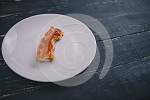 A small piece or bite of pie, leftover on white plate on black wooden table