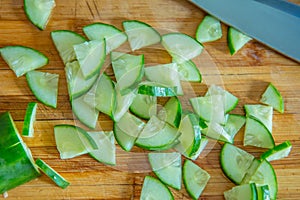 Small pieces of cucumber for salad on a wooden cutting board and cook knife