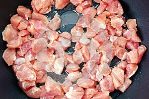 Small pieces of pork meat are fried in a pan in olive oil. close up selective focus